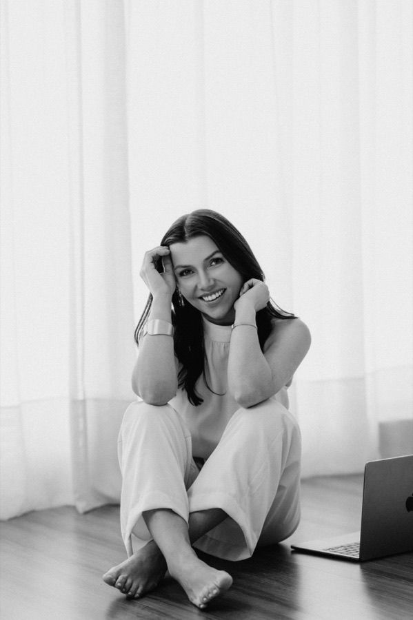 Dra. Letícia Melo sorrindo, sentada no chão ao lado do notebook